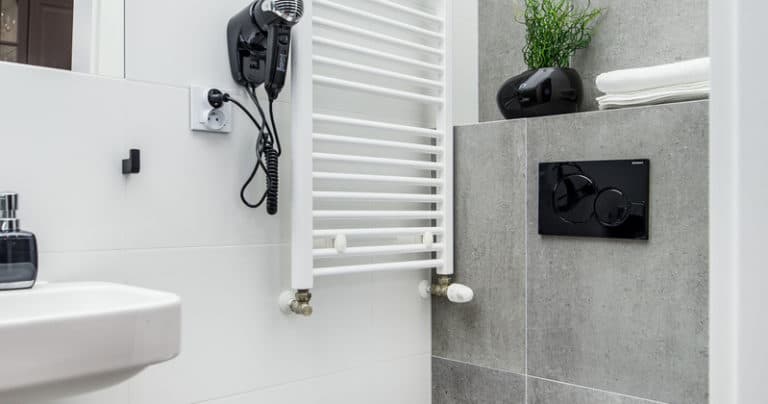 Compact bathroom featuring wall-mounted hairdryer, white towel radiator and grey tiled toilet panel