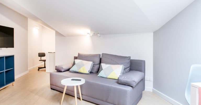 Cozy gray leather sofa with patterned throw pillows and a small round white coffee table.