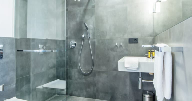 Modern grey bathroom showing walk-in shower, wall-mounted sink, towel rail and muted lighting.